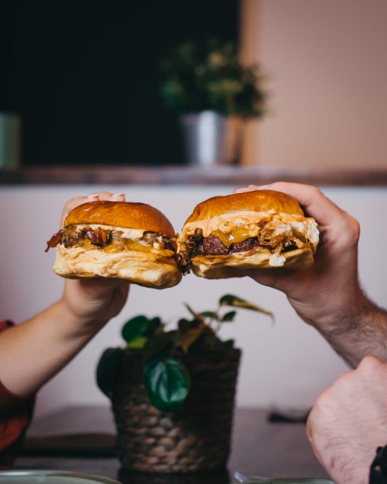 Dos personas brindando con sendas hamburguesas sobre la mesa de un local