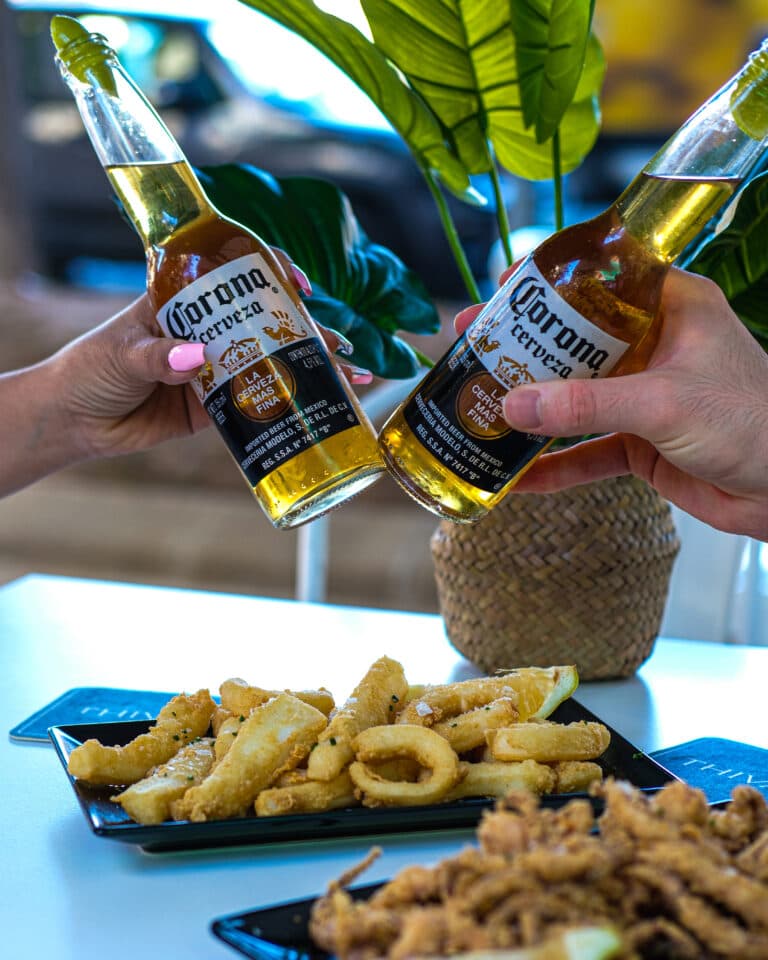 Brindis amb dues cerveses sobre una taula amb fregits per compartir